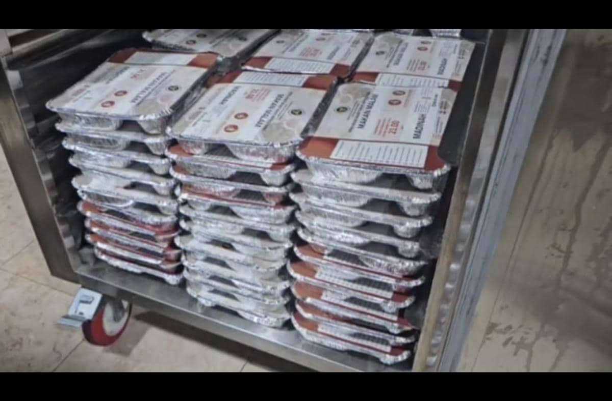 Tumpukan paket makanan dalam wadah aluminium siap saji yang disusun rapi di rak logam untuk jemaah haji Indonesia.