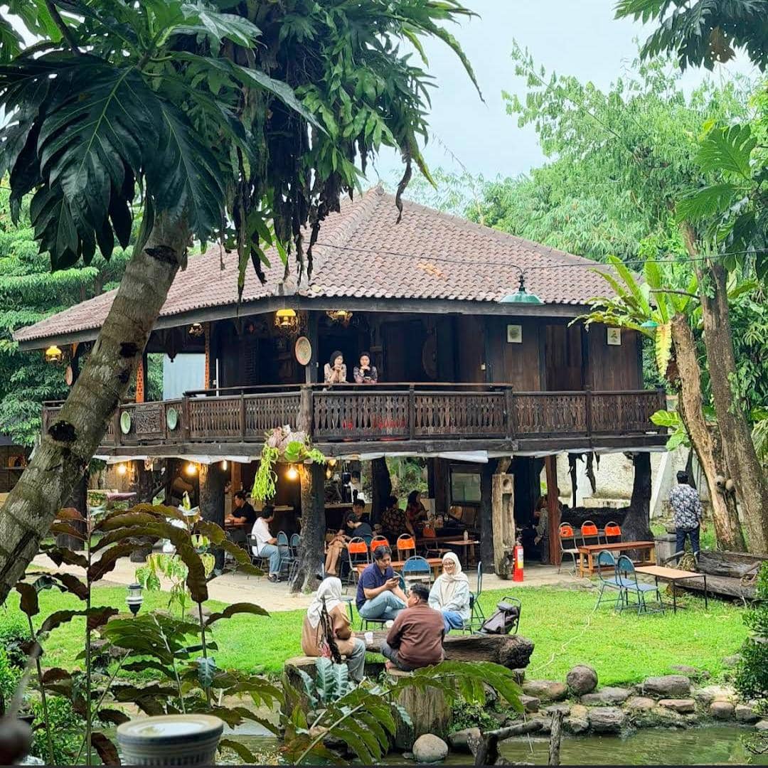 Suasana Kopi Merbaoe di Bandar Lampung dengan bangunan kayu tradisional dan pengunjung yang menikmati waktu di area hijau terbuka.
