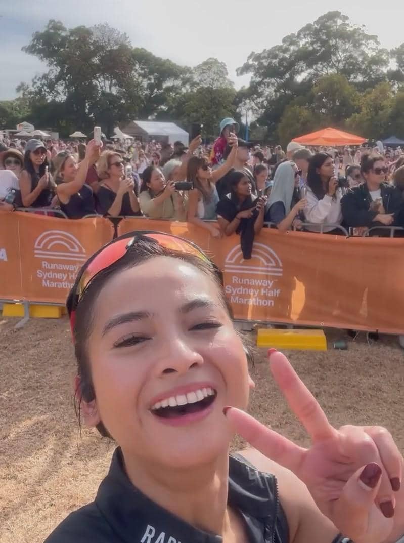 Seorang pelari tersenyum sambil berpose dengan tanda damai di depan kerumunan penonton di ajang Runaway Sydney Half Marathon.