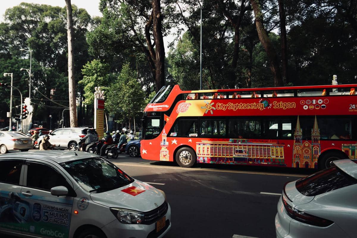 Ilustrasi bus wisata melewati ikon kota Surabaya seperti museum dan kawasan pusat kota.