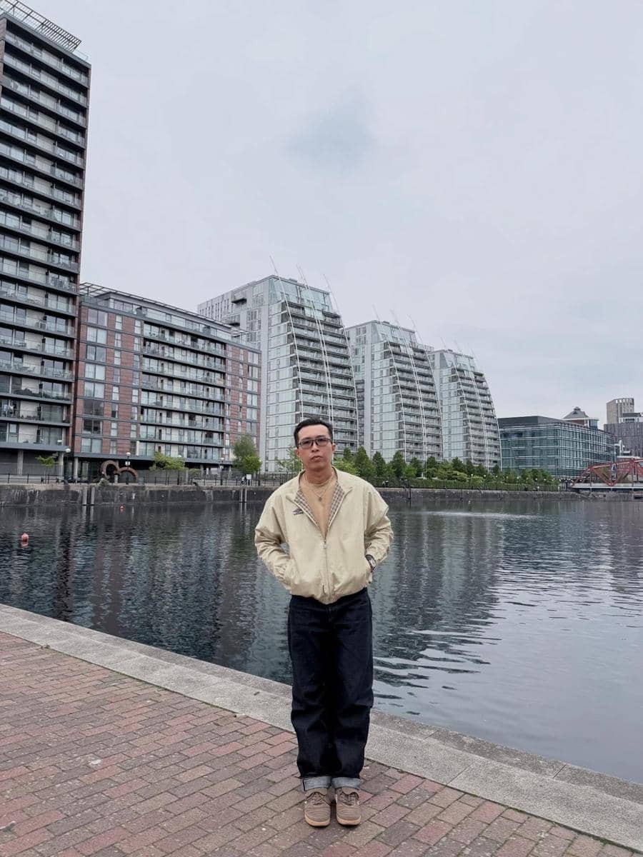dr. Tirta berdiri di tepi danau dengan latar gedung-gedung modern bertingkat di kawasan perkotaan dekat Old Trafford.