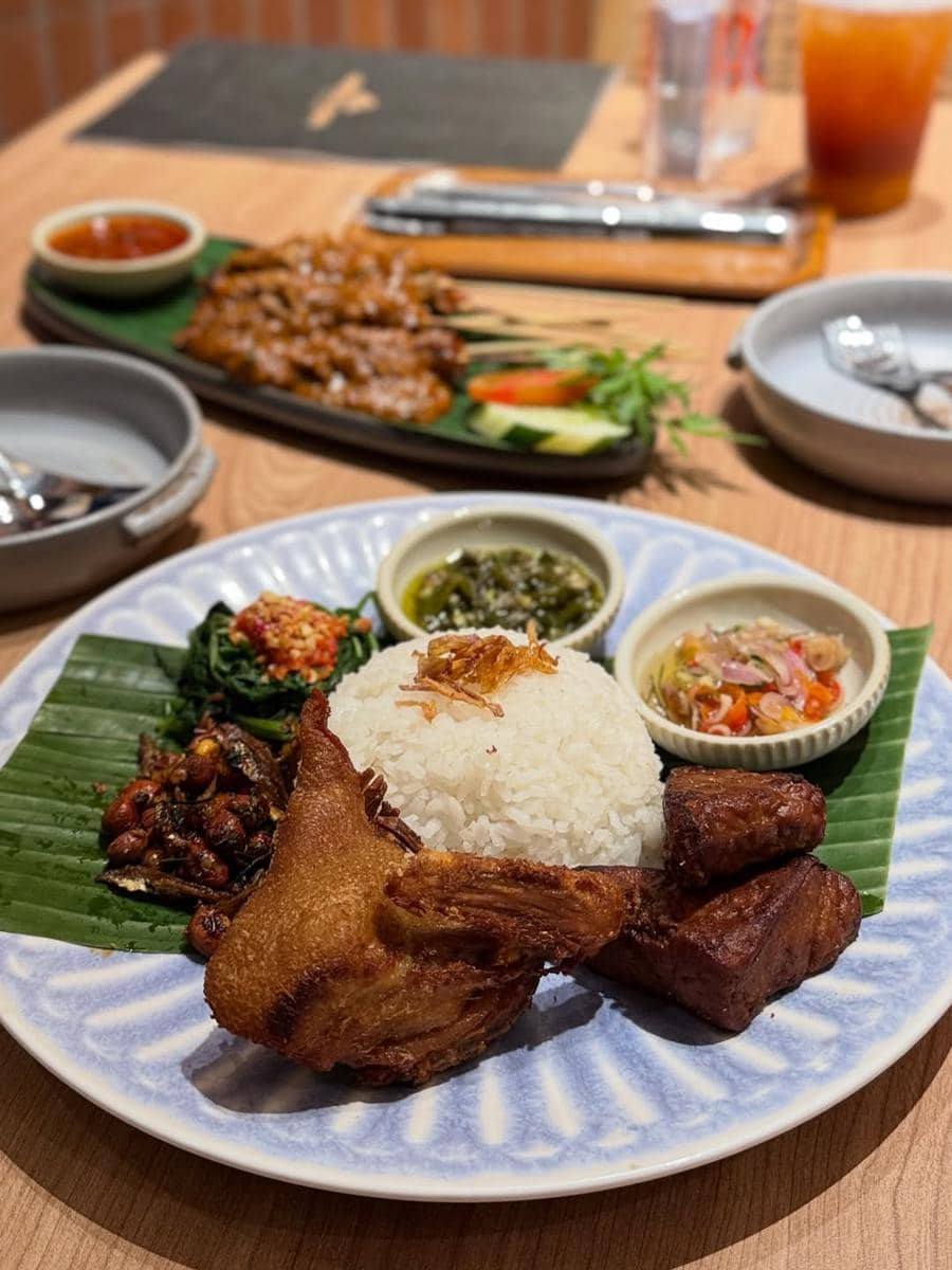 Hidangan nasi putih dengan ayam goreng, tempe goreng, sambal, dan lalapan disajikan di atas piring di Cafe Resto Aneka Sari Dapur Rasa Bandar Lampung.