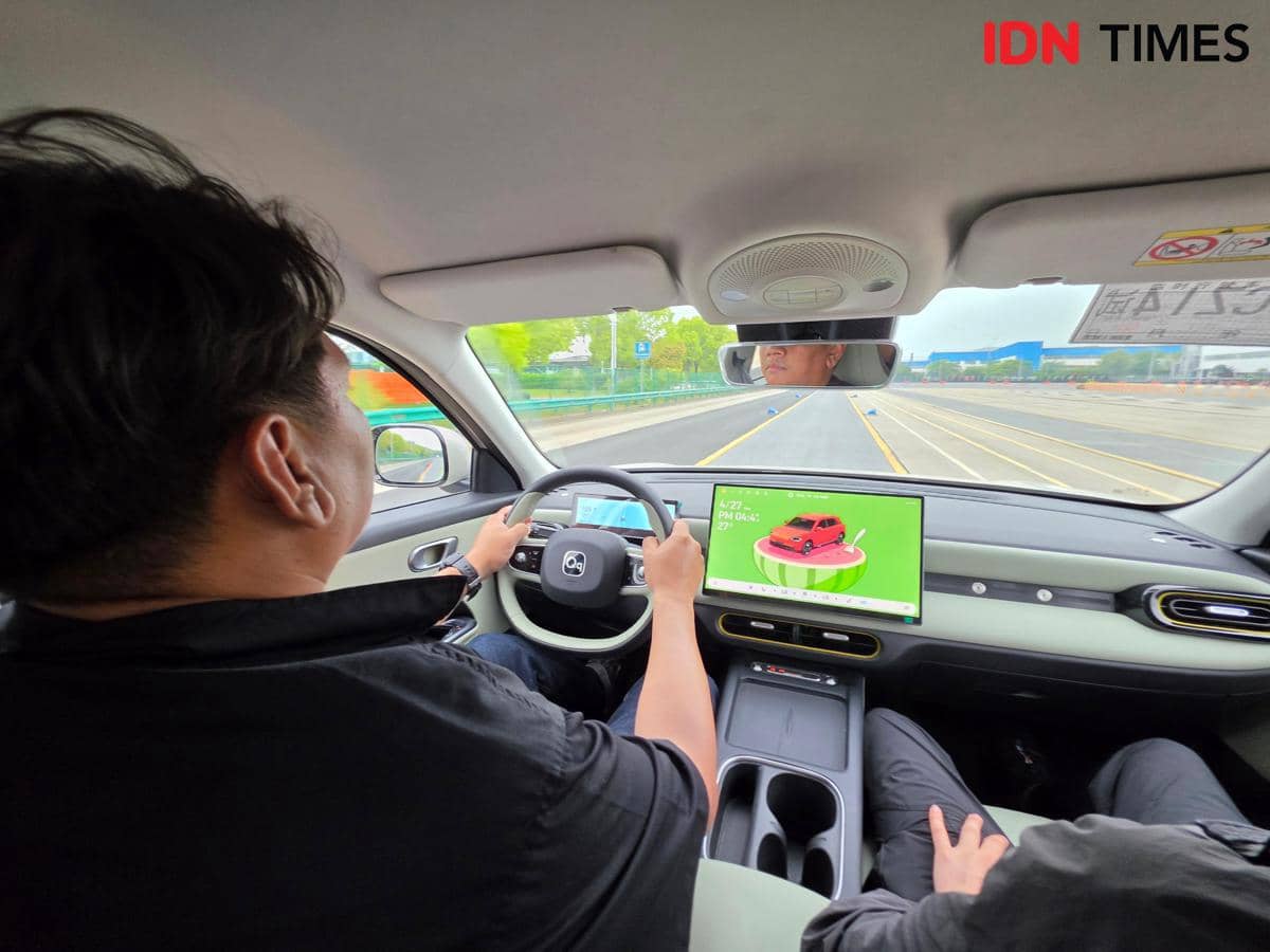 Seorang pengemudi mengendarai mobil Chery Q di jalan uji dengan layar digital besar menampilkan tampilan kendaraan di dasbor.