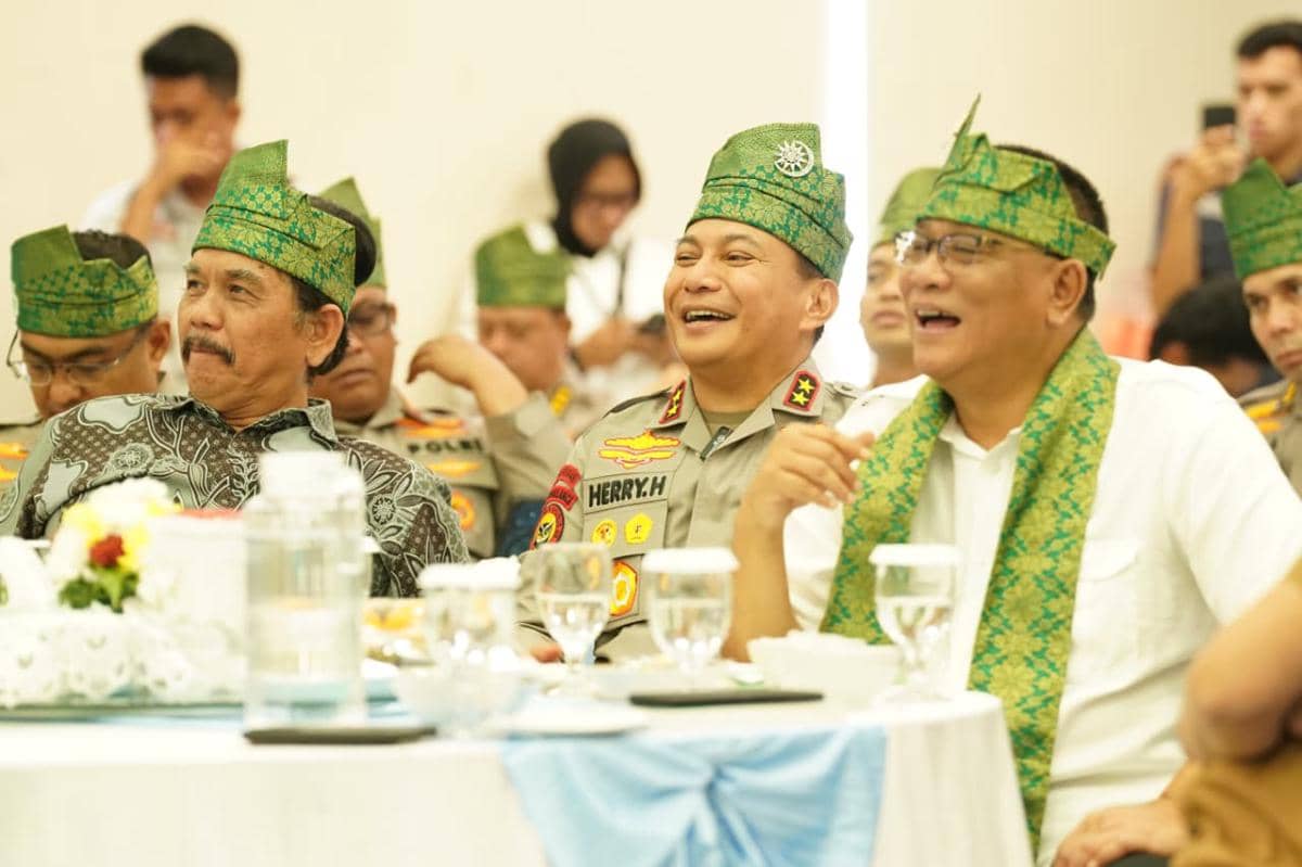 Beberapa pejabat mengenakan tanjak hijau duduk bersama dan tersenyum saat acara kunjungan kerja di Polda Riau.