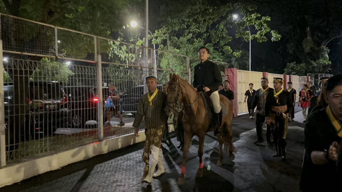 Seorang pria berpakaian adat menunggang kuda diiringi rombongan berjalan di area Stadion Manahan Solo pada malam hari.
