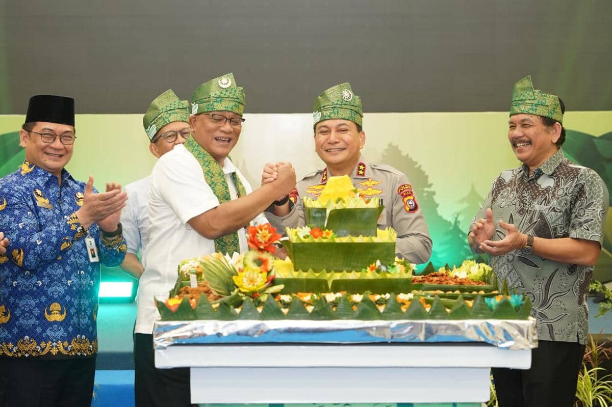 Beberapa pejabat mengenakan tanjak hijau berdiri di depan tumpeng besar saat kunjungan kerja ke Polda Riau pada awal Mei 2026.