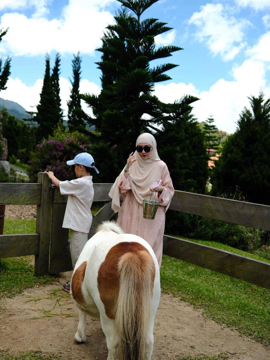 Larissa Chou dan anak kecil berada di area peternakan kecil bersama seekor kuda poni di bawah langit cerah.