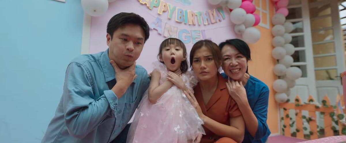 Empat orang, termasuk seorang anak kecil bergaun pink, berpose dengan ekspresi lucu di pesta ulang tahun bertema warna pastel.
