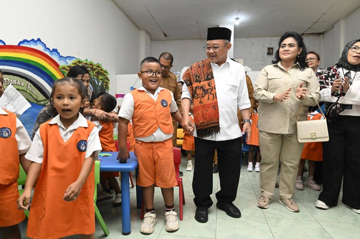 Seorang pejabat pendidikan mengunjungi taman kanak-kanak di Kupang, berinteraksi dengan anak-anak yang mengenakan seragam oranye.