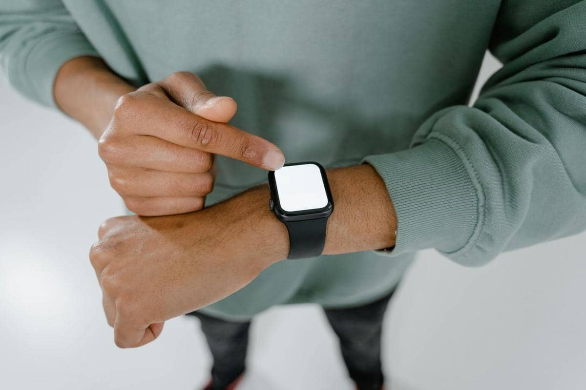 Seseorang mengenakan smartwatch dengan layar kosong di pergelangan tangan sambil menyentuh layarnya menggunakan jari telunjuk.