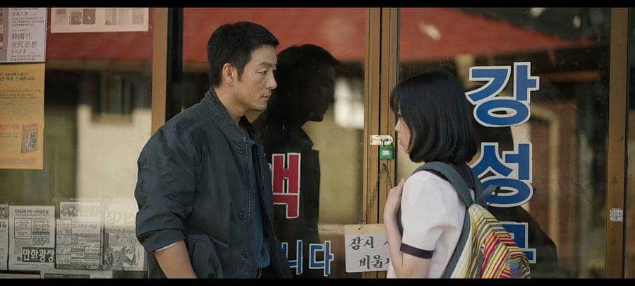 Seorang pria dan siswi berseragam berdiri saling berhadapan di depan toko dengan kaca dan tulisan Korea, adegan dari drama The Scarecrow.