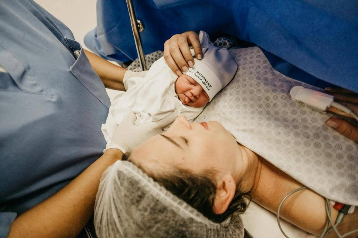 Seorang bidan sedang menggendong bayi yang baru saja lahir, lalu memperlihatkannya kepada sang ibu.