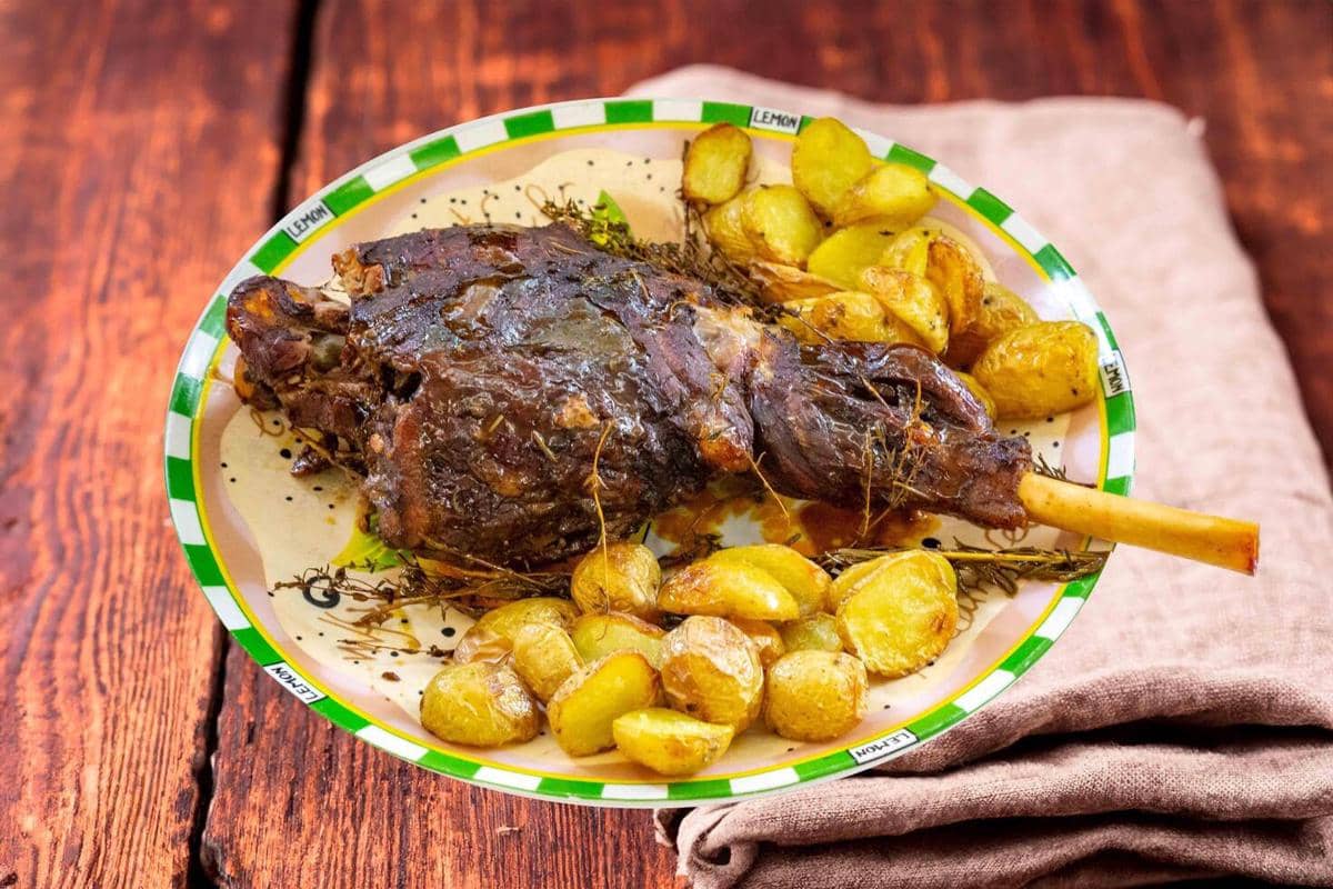 Hidangan daging panggang ala Maroko disajikan di piring dengan kentang panggang dan rempah di atas meja kayu.