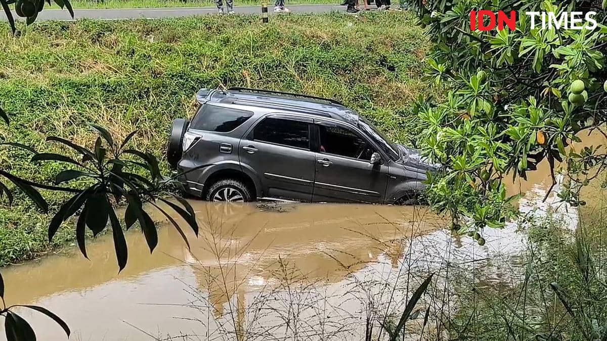 Sebuah minibus berwarna hitam terperosok ke dalam parit berair cokelat di dekat Bandara Soekarno-Hatta, sebagian badan mobil terendam.