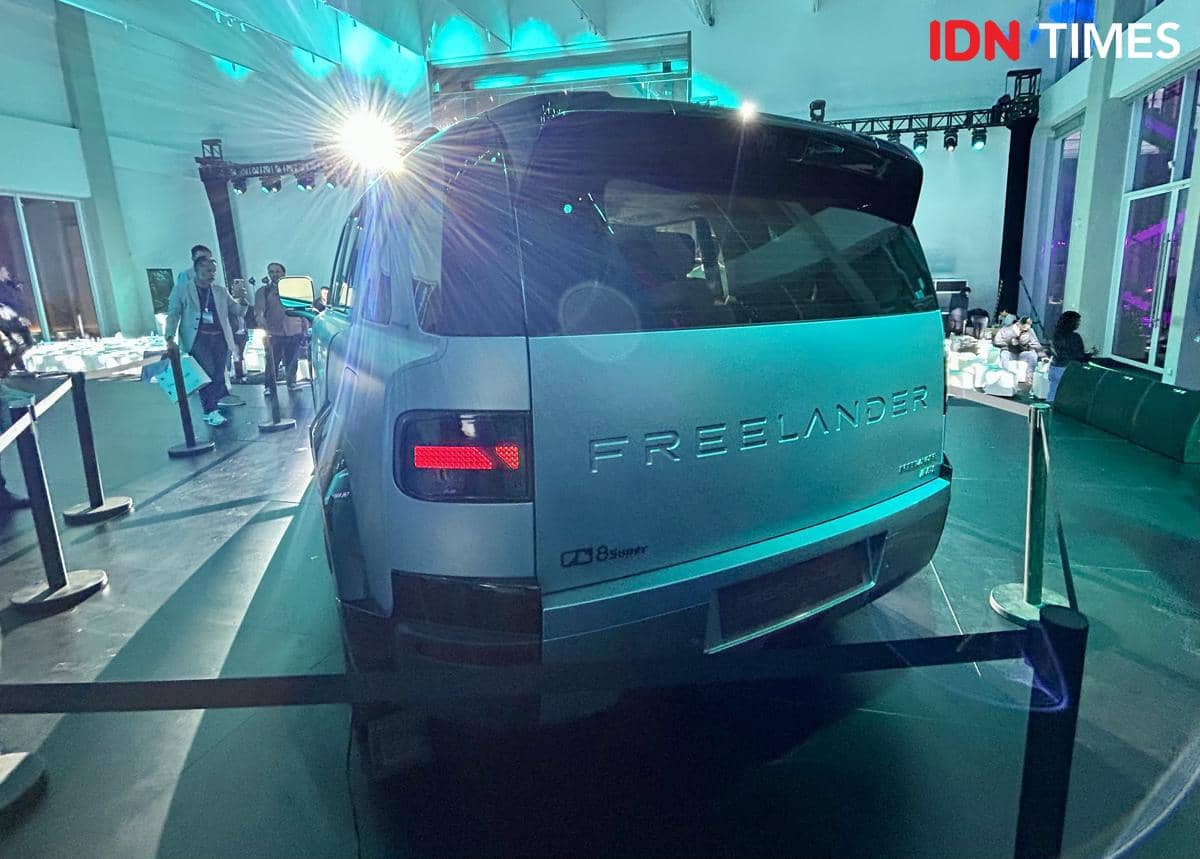 Tampak belakang mobil Freelander 8 berwarna perak dipamerkan di ruangan dengan pencahayaan biru dan pengunjung di sekitarnya.