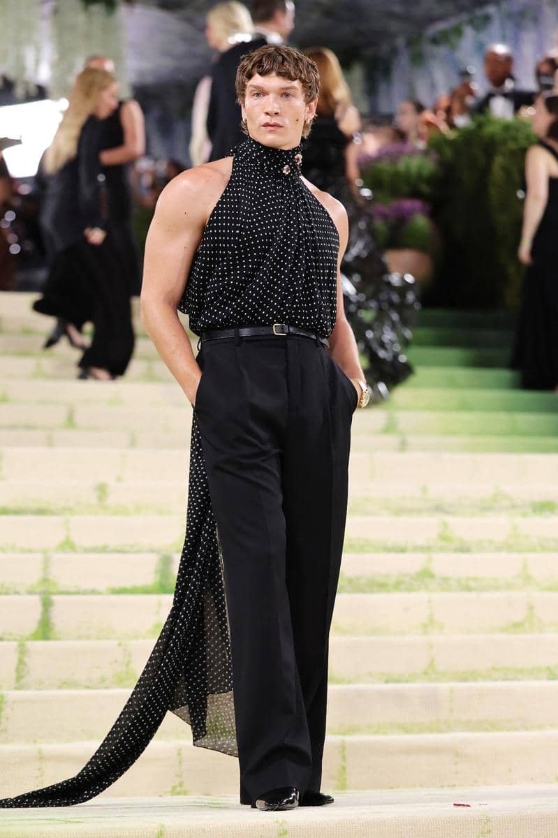 Connor Storie mengenakan atasan tanpa lengan bermotif polkadot dan celana panjang hitam berpose di tangga acara Met Gala 2026.
