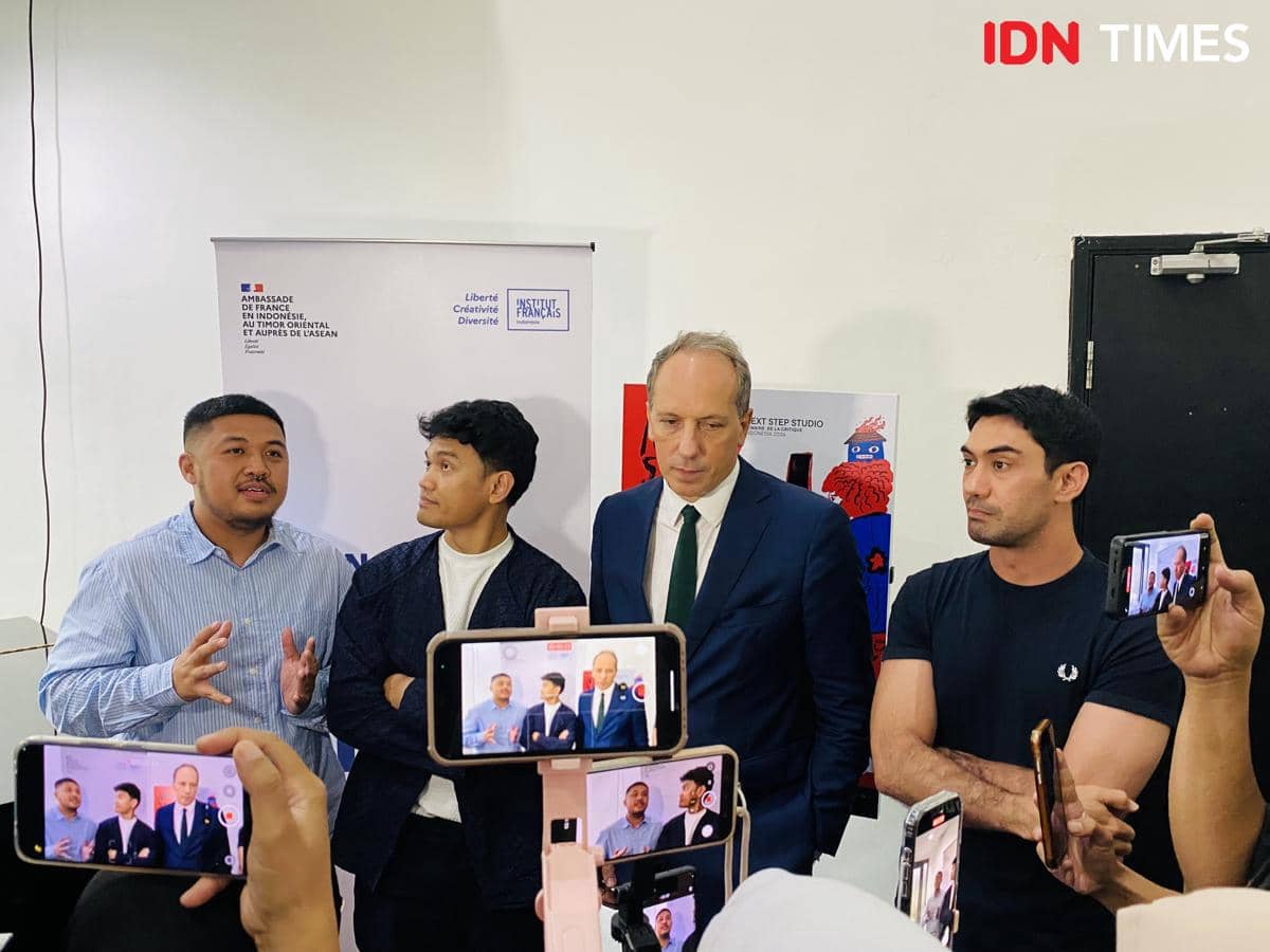 Beberapa pria berbicara di depan media saat konferensi pers Next Step Studio Indonesia dengan latar spanduk dan kamera ponsel merekam.