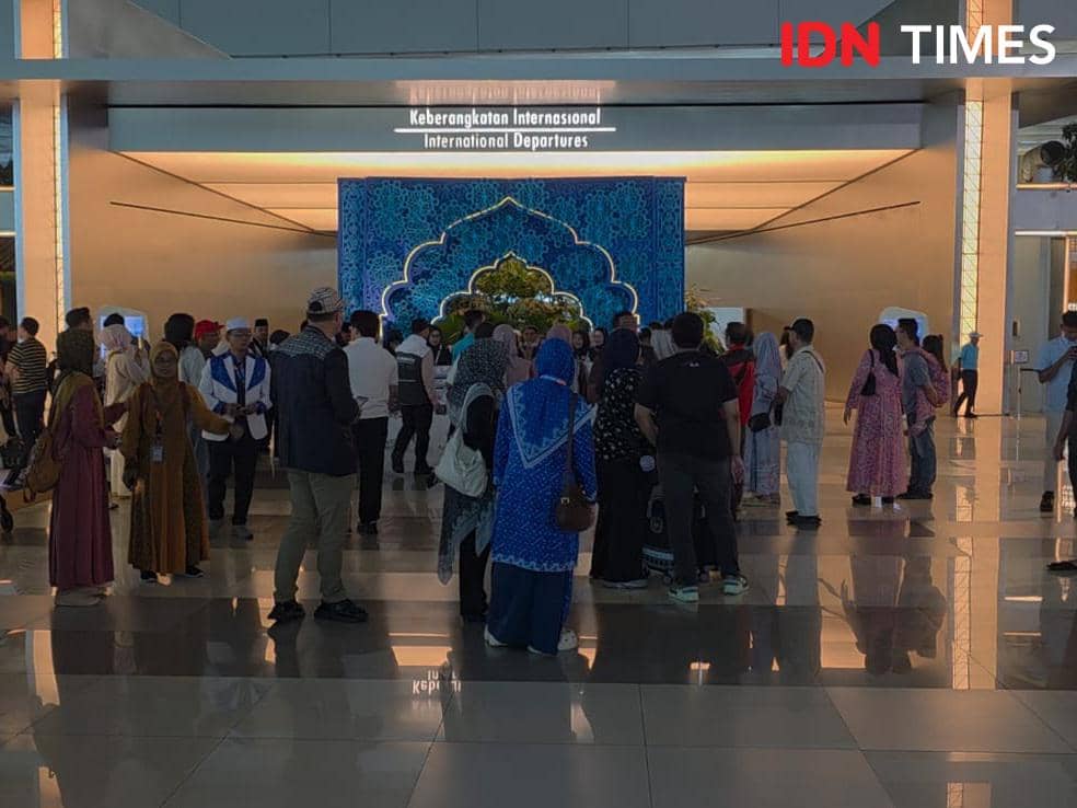 Sejumlah orang berkumpul di area keberangkatan internasional Bandara Soekarno-Hatta dengan latar dekorasi bertema haji.