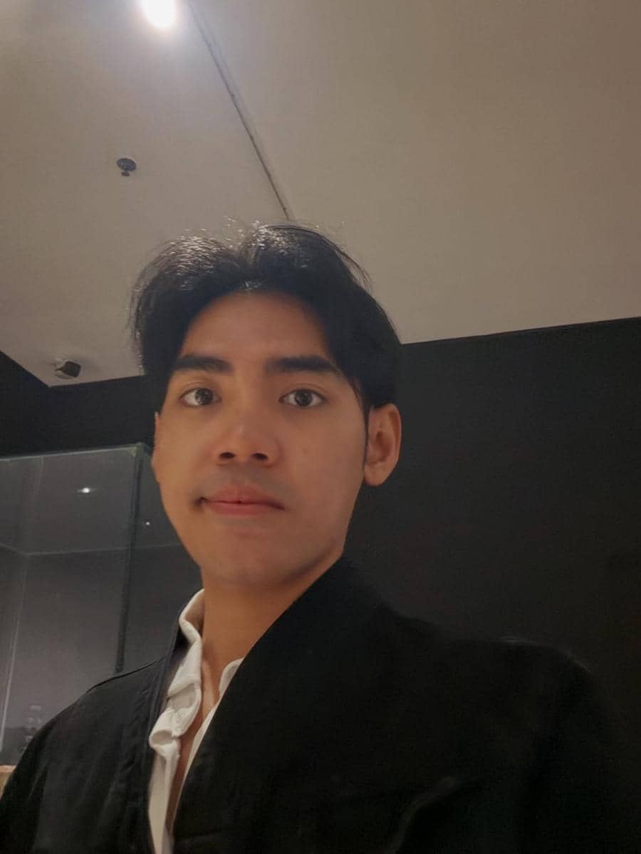dr. Ikhsan mengenakan kemeja putih dan jaket hitam berfoto selfie di dalam ruangan dengan pencahayaan hangat.