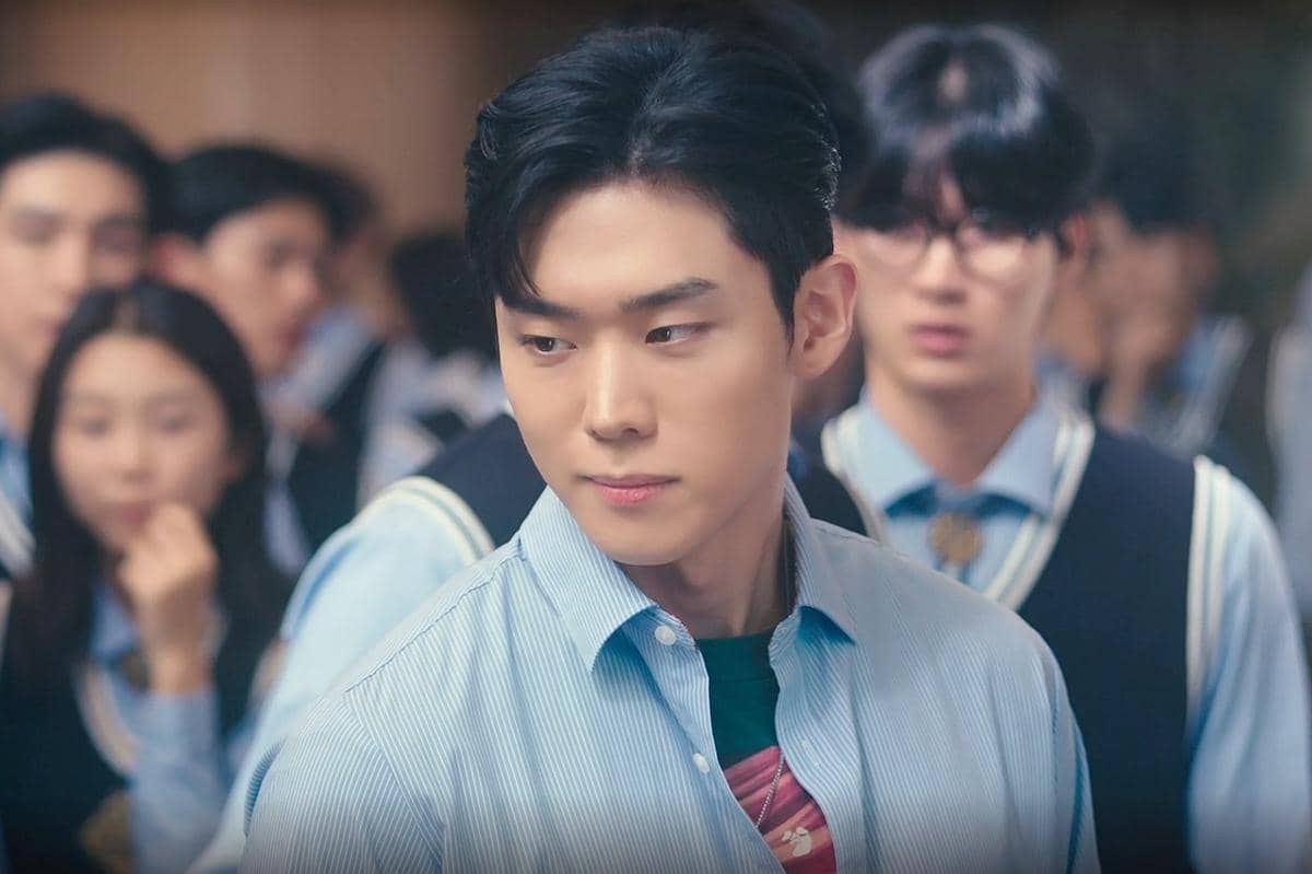 Seorang siswa laki-laki mengenakan kemeja biru muda berdiri di antara teman-teman sekolahnya dalam adegan drama Korea Perfect Crown.