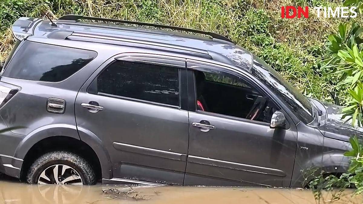 Sebuah minibus berwarna abu-abu terperosok ke dalam parit berlumpur di sekitar Bandara Soekarno-Hatta dengan kondisi sebagian terendam air.