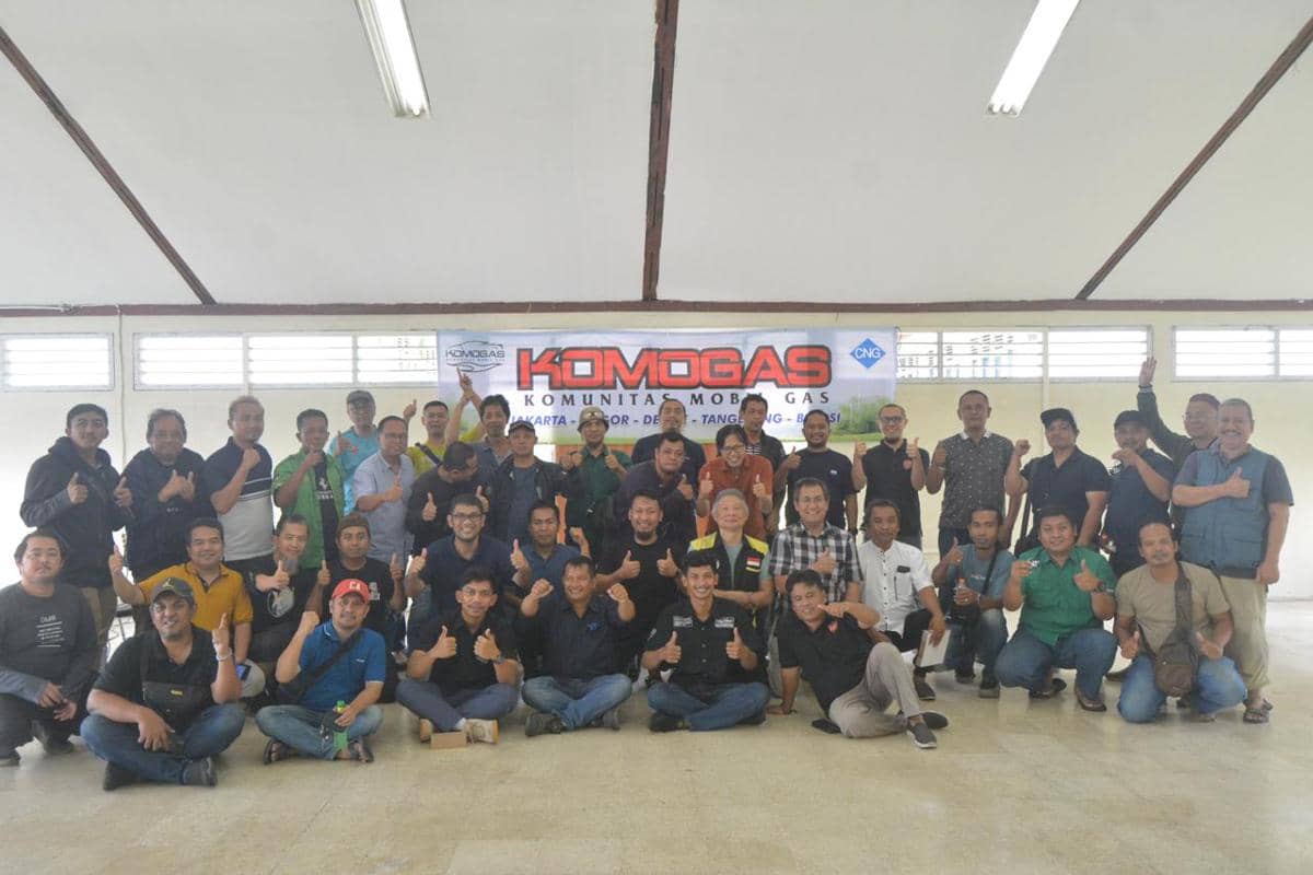 Anggota Komunitas Mobil Gas berfoto bersama di dalam ruangan dengan latar spanduk bertuliskan KOMOGAS dan logo CNG.