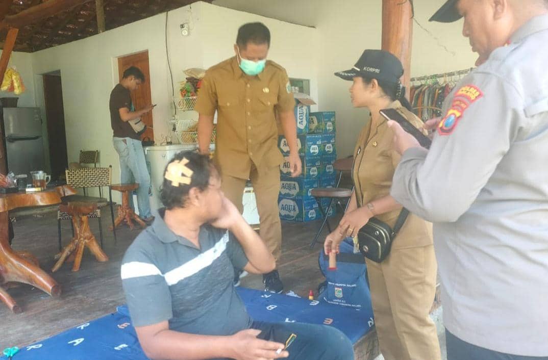 Petugas berbicara dengan seorang pria yang mengalami luka di kepala dan duduk di teras rumah setelah insiden di Pantai Wedi Awu.