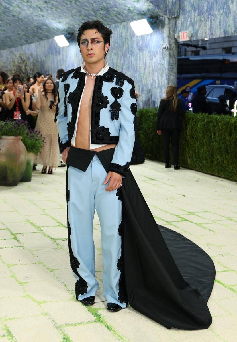 Hudson Williams mengenakan setelan biru muda dengan hiasan hitam dan jubah panjang hitam saat berjalan di karpet Met Gala 2026.