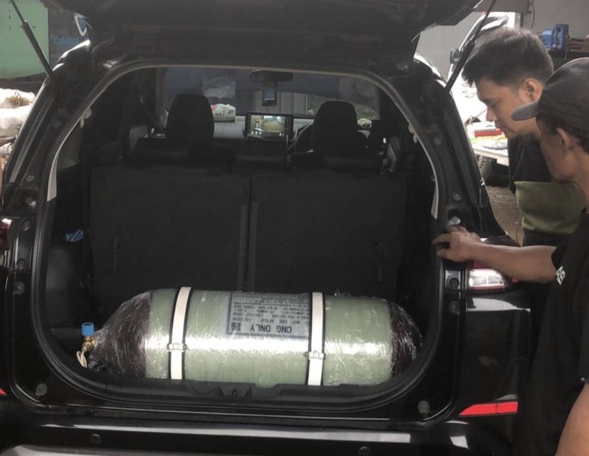 Dua orang memeriksa tabung gas BBG yang terpasang di bagasi mobil berwarna hitam dengan pintu belakang terbuka.
