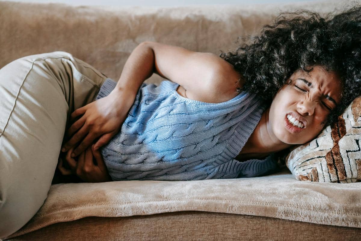Seorang wanita berbaring di sofa sambil memegangi perutnya dengan ekspresi kesakitan, menggambarkan gejala sakit perut akibat hantavirus.