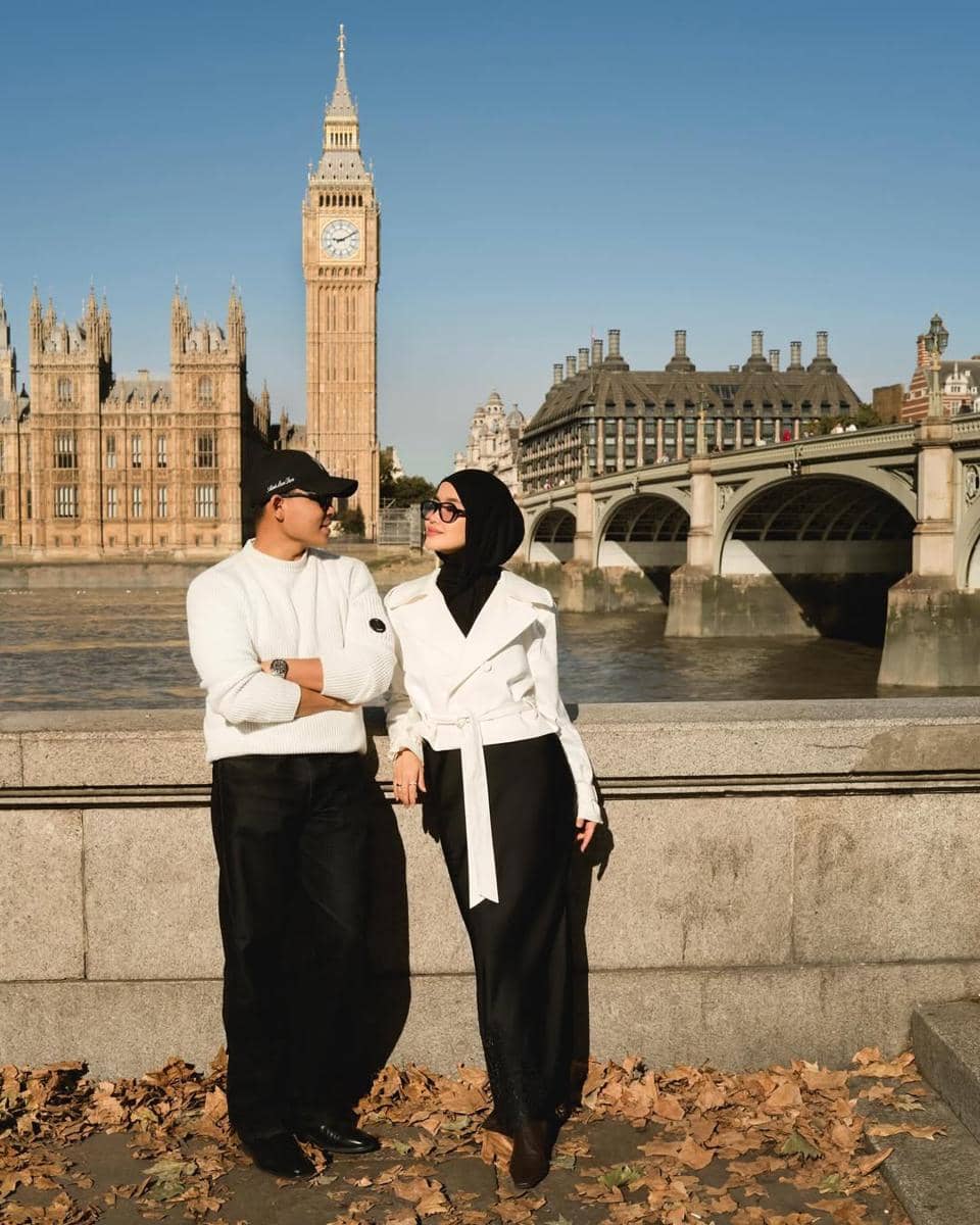 Sepasang pria dan wanita bergaya modis dengan latar belakang Big Ben dan Sungai Thames di London pada hari cerah.