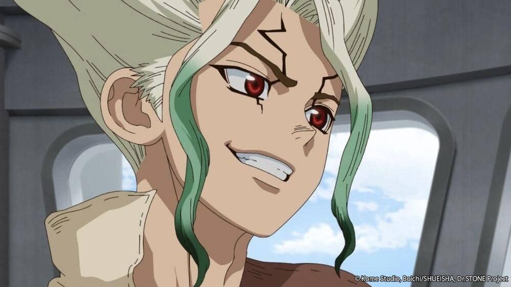 Senku, karakter anime berambut putih dengan ujung hijau dan mata merah, tersenyum percaya diri di dalam ruangan dengan jendela besar.