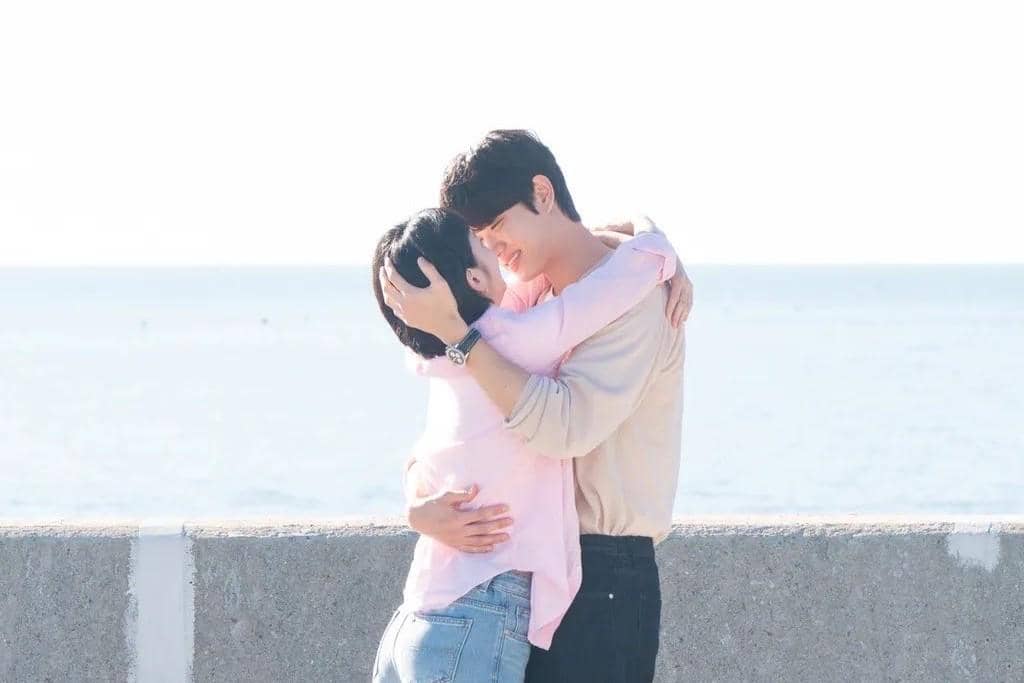 Sepasang pria dan wanita berpelukan hangat di tepi laut dengan latar langit cerah dalam cuplikan drama Yumi's Cells 3.