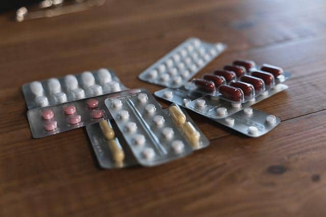 Beberapa blister berisi berbagai jenis obat dengan warna dan bentuk berbeda diletakkan di atas meja kayu.