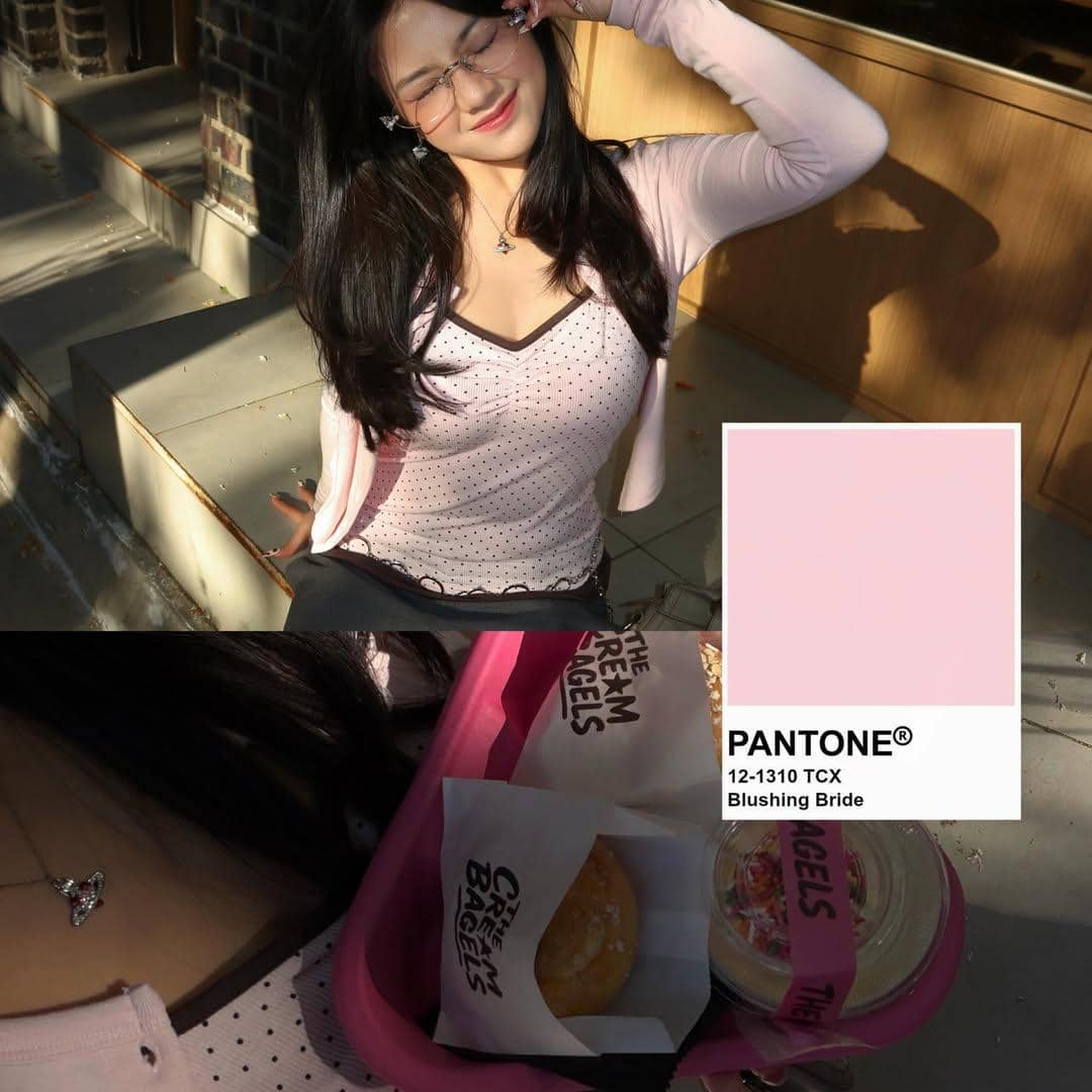 Seorang wanita berpose sambil tersenyum di bawah sinar matahari, mengenakan atasan pink muda dengan baki berisi dessert dan minuman.