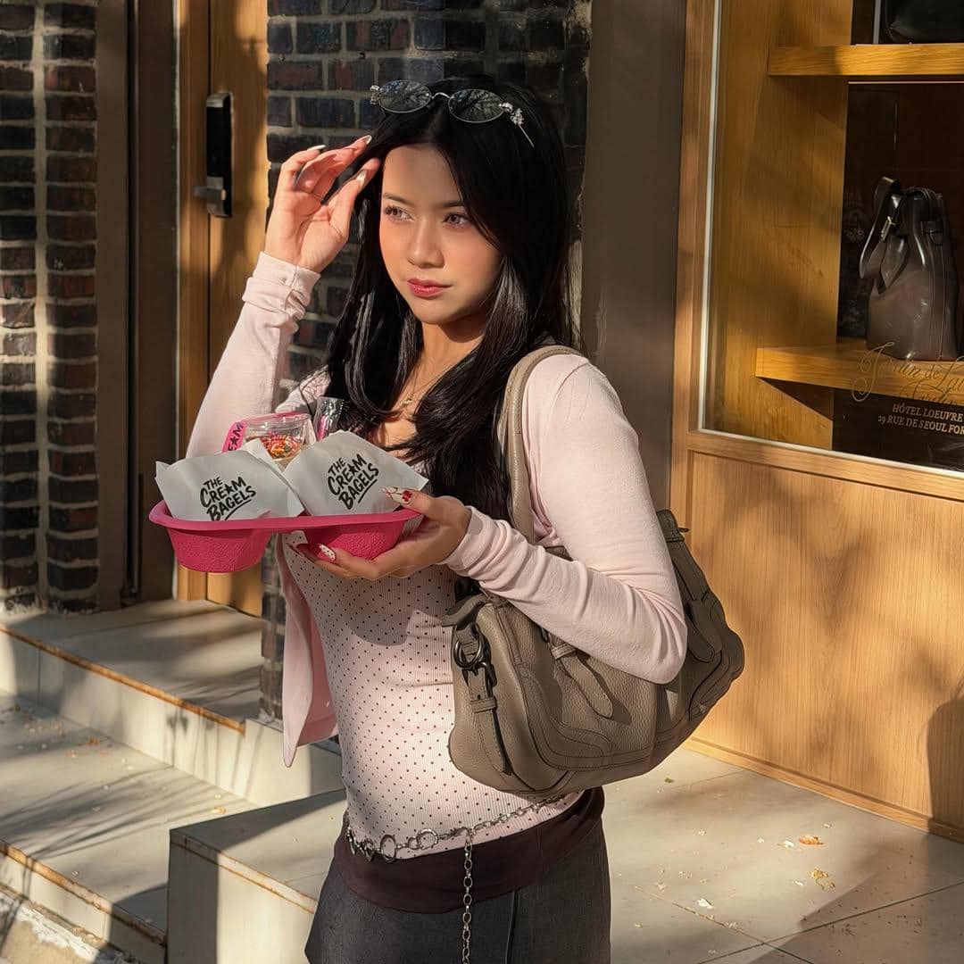 Seorang wanita mengenakan pakaian berwarna lembut membawa dua dessert dalam wadah merah muda di depan toko di Seoul.