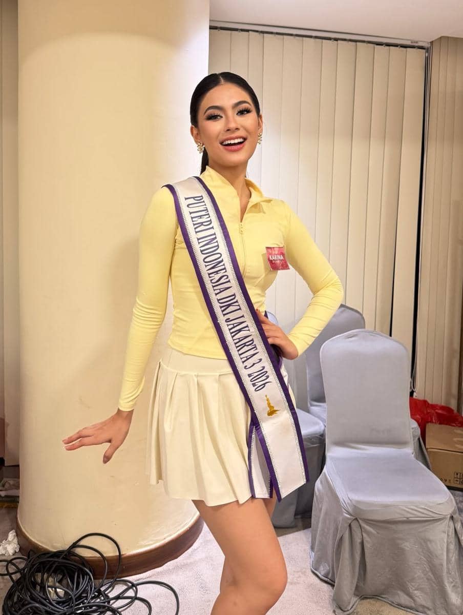 Seorang perempuan mengenakan selempang bertuliskan Puteri Indonesia Jakarta 3 2026, berpose sambil tersenyum di dalam ruangan.