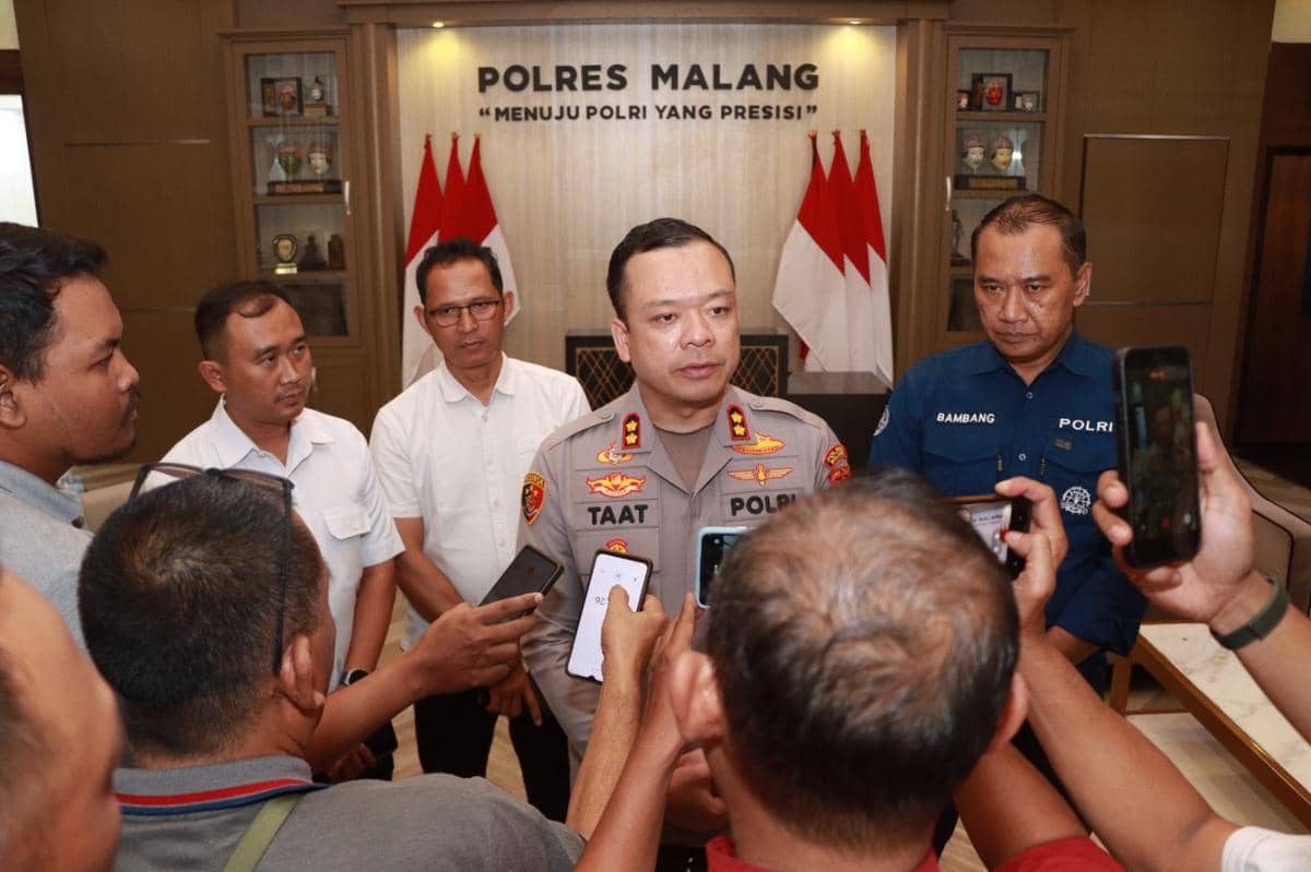 Seorang perwira polisi berpakaian dinas memberikan keterangan kepada sejumlah wartawan di kantor Polres Malang dengan latar bendera merah putih.