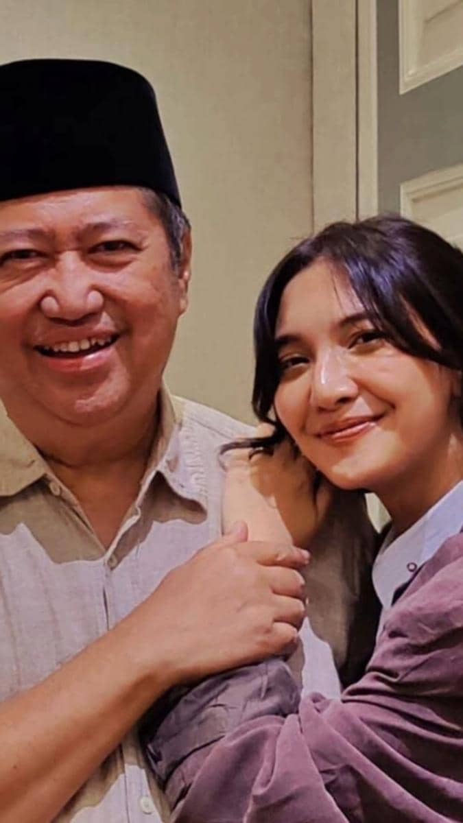 Seorang pria mengenakan peci hitam tersenyum berdampingan dengan seorang wanita berambut panjang yang juga tersenyum hangat.