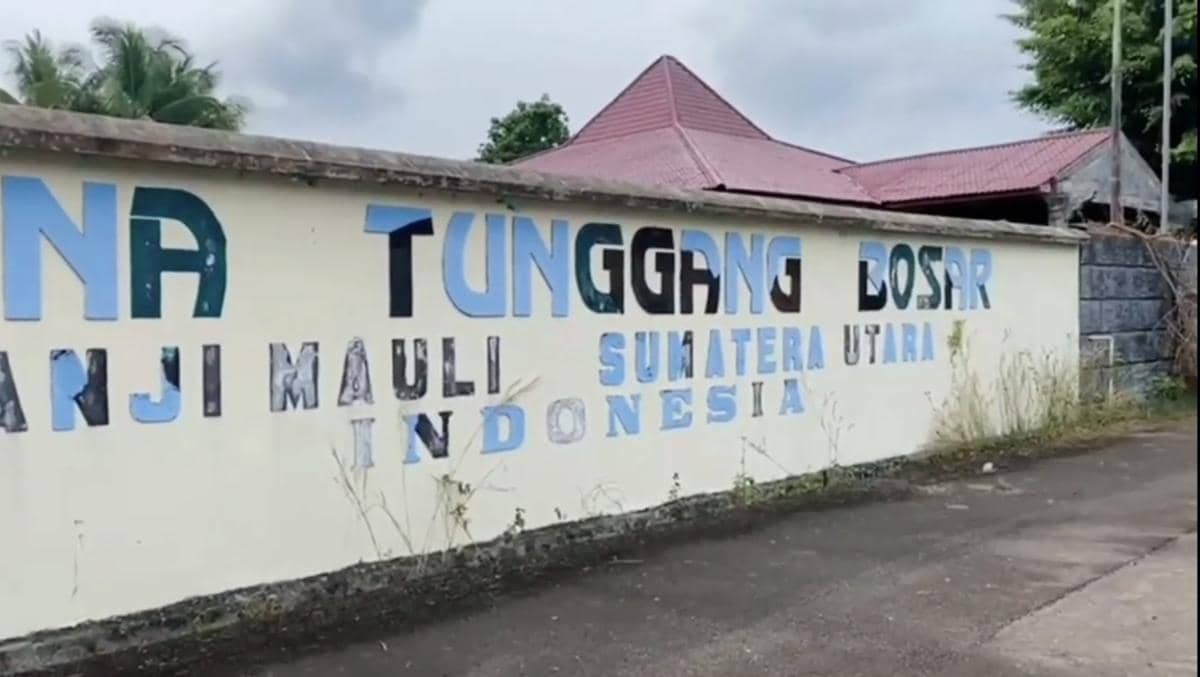 Tembok dengan tulisan Istana Tunggang Bosar di Panji Mauli, Sumatera Utara, Indonesia, dengan bangunan beratap merah di belakangnya.