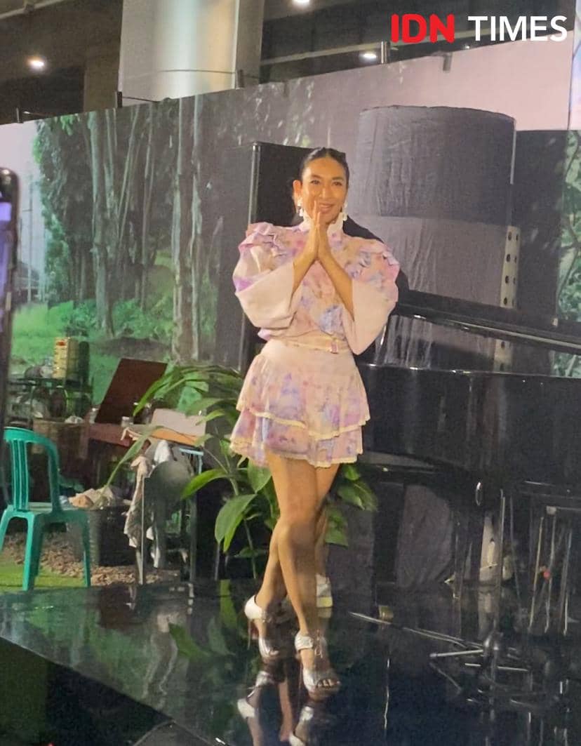 Seorang pemain film mengenakan gaun bermotif pastel berpose di atas panggung saat gala premier film Semua Akan Baik-Baik Saja.