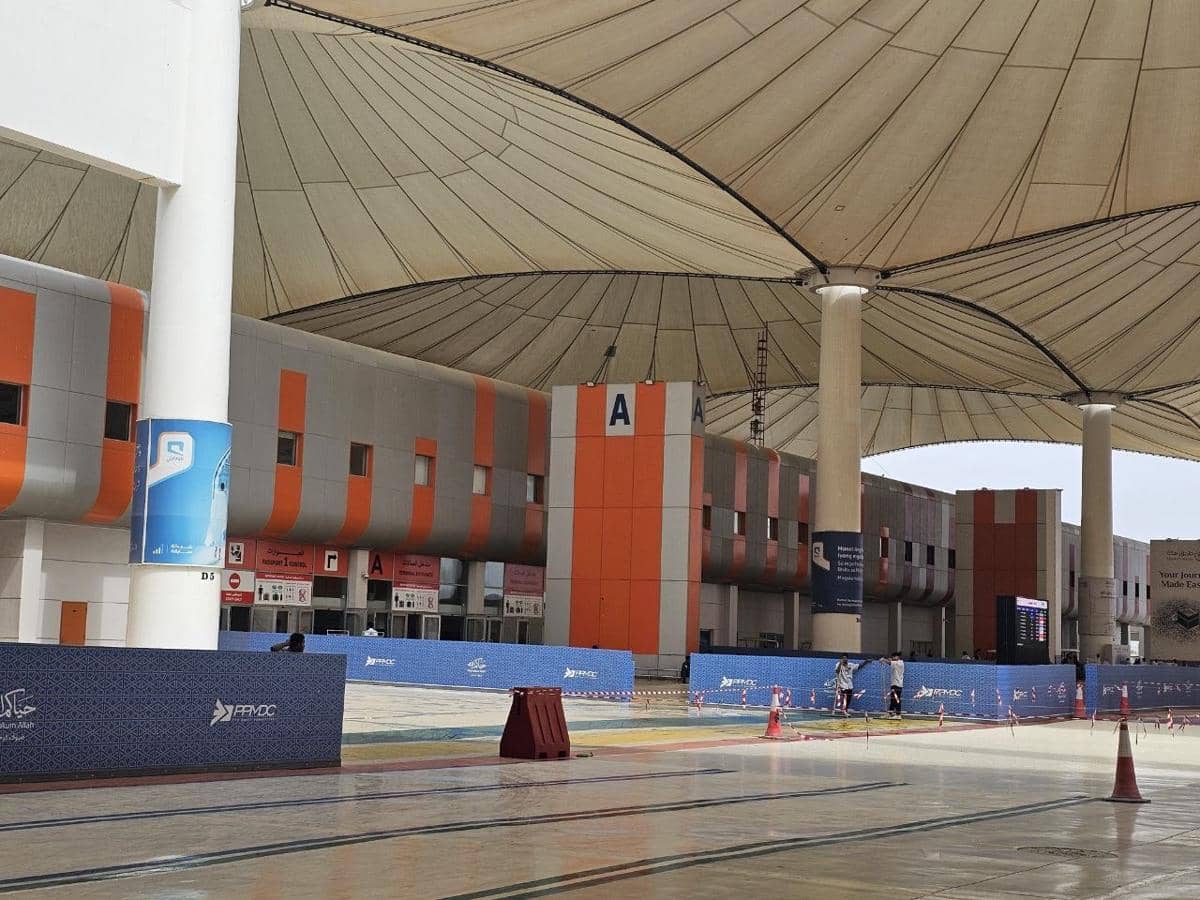 Gerbang A di Bandara Internasional King Abdul Aziz Jeddah dengan atap kanopi besar dan area luar yang luas di bawah sinar matahari.