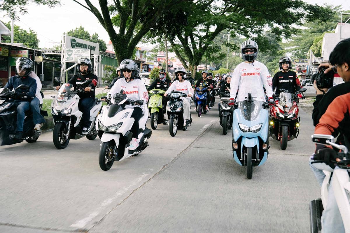 Sekelompok pengendara motor skuter berkendara bersama di jalan kota Bogor dengan suasana ramai dan pepohonan rindang di tepi jalan.