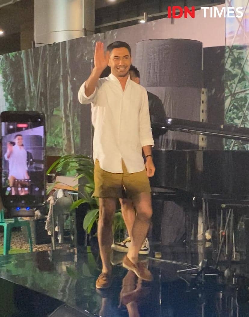 Seorang pemain film mengenakan kemeja putih dan celana pendek cokelat melambaikan tangan di gala premier film Semua Akan Baik-Baik Saja.