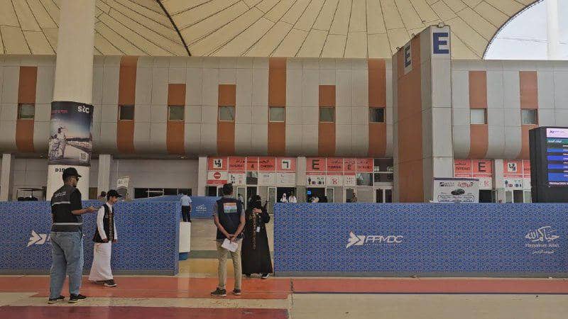 Beberapa orang berdiri di area Gate E Bandara King Abdul Aziz Jeddah dengan latar bangunan modern dan atap melengkung besar.