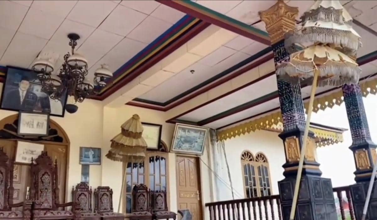 Bagian dalam Istana Tunggang Bosar dengan kursi ukir kayu, lampu gantung klasik, dan ornamen tradisional di langit-langit serta tiang.
