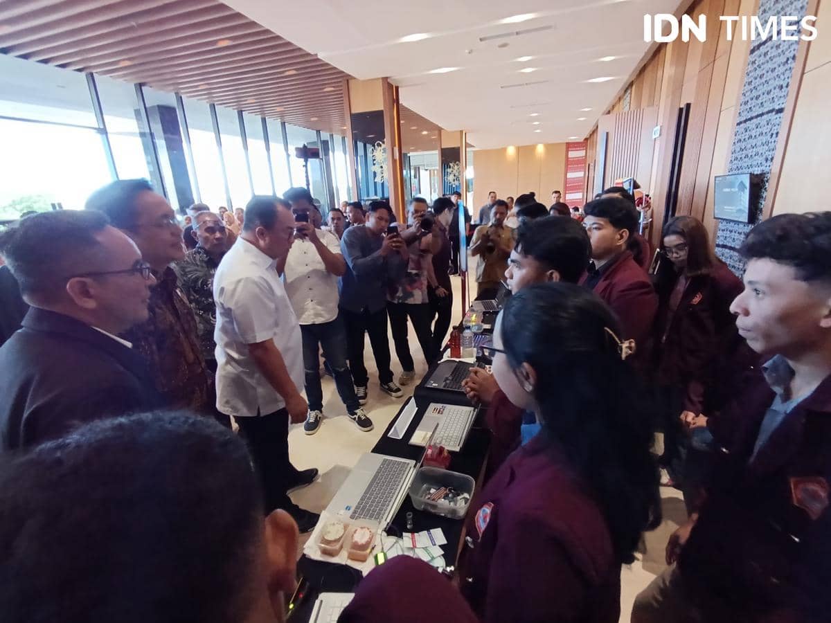 Kepala BRIN meninjau stan inovasi teknologi mahasiswa di Kupang, berinteraksi dengan peserta yang mengenakan jas almamater marun.
