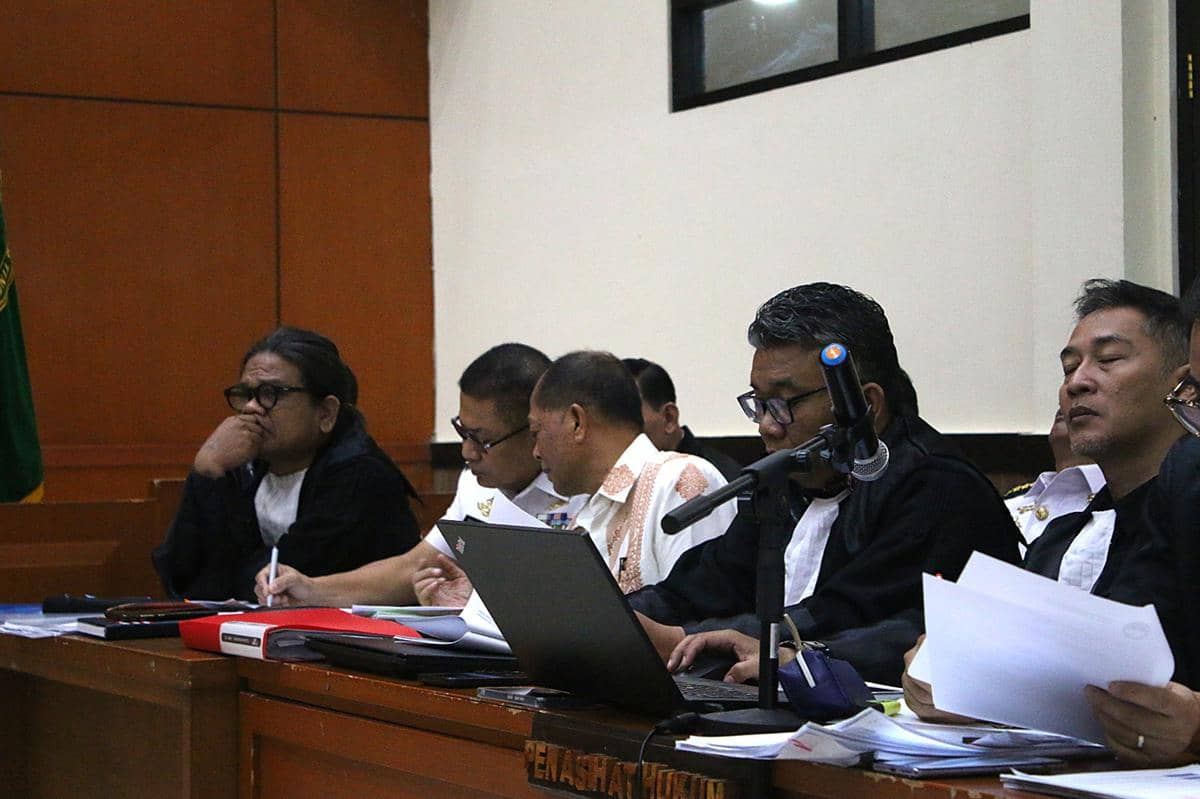 Beberapa pria duduk di ruang sidang dengan berkas dan laptop di meja, mengikuti sidang kasus korupsi satelit Kementerian Pertahanan.