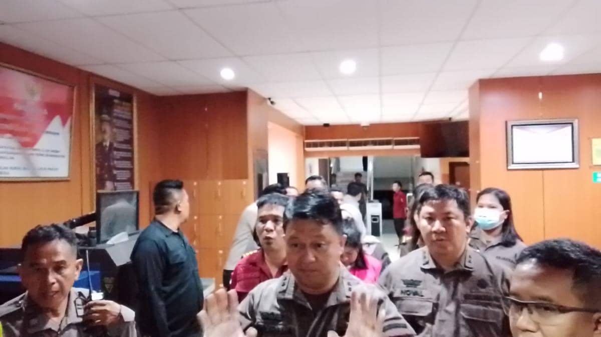 Petugas Kejati Sulut mengawal seorang perempuan berpakaian merah menuju mobil tahanan di dalam gedung berpanel kayu.