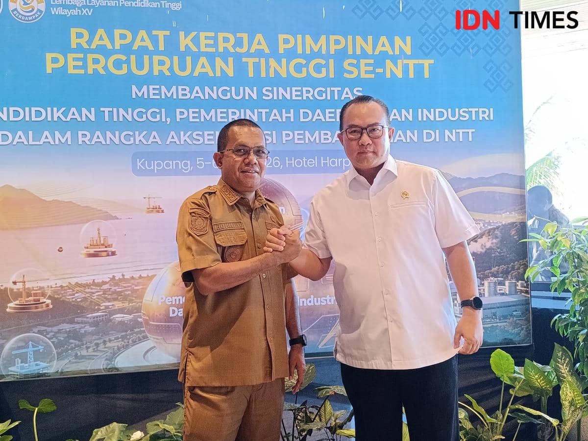 Dua pria berjabat tangan di depan backdrop rapat kerja pimpinan perguruan tinggi se-NTT di Kupang dengan tema sinergi pendidikan dan industri.